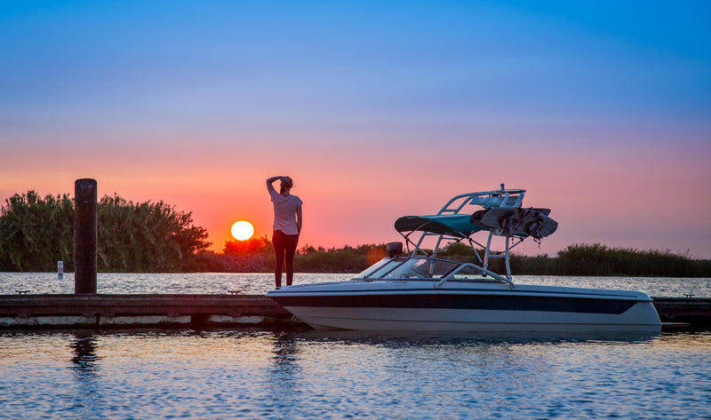 Boat with wakeboard tower docked at sunset.